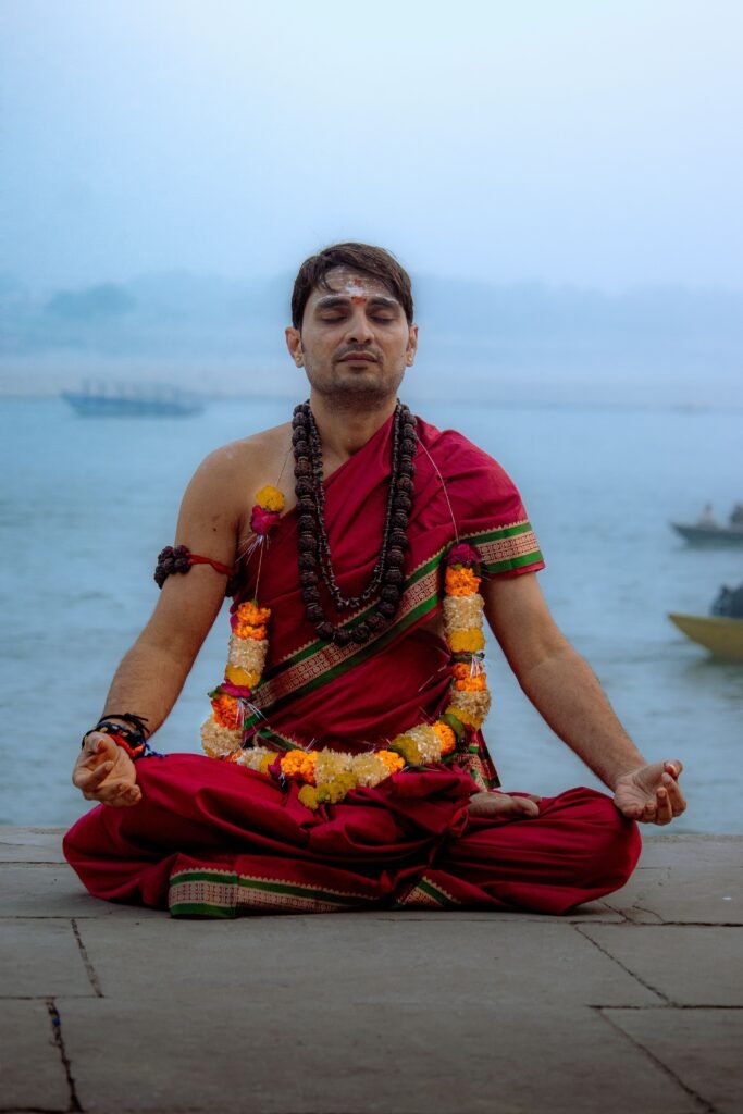 A yogi meditates by the river in traditional attire, promoting peace and mindfulness.